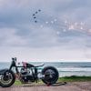 Royal Enfield sprint racing motorcycle on Biarritz beach with jet aircraft doing fly-by